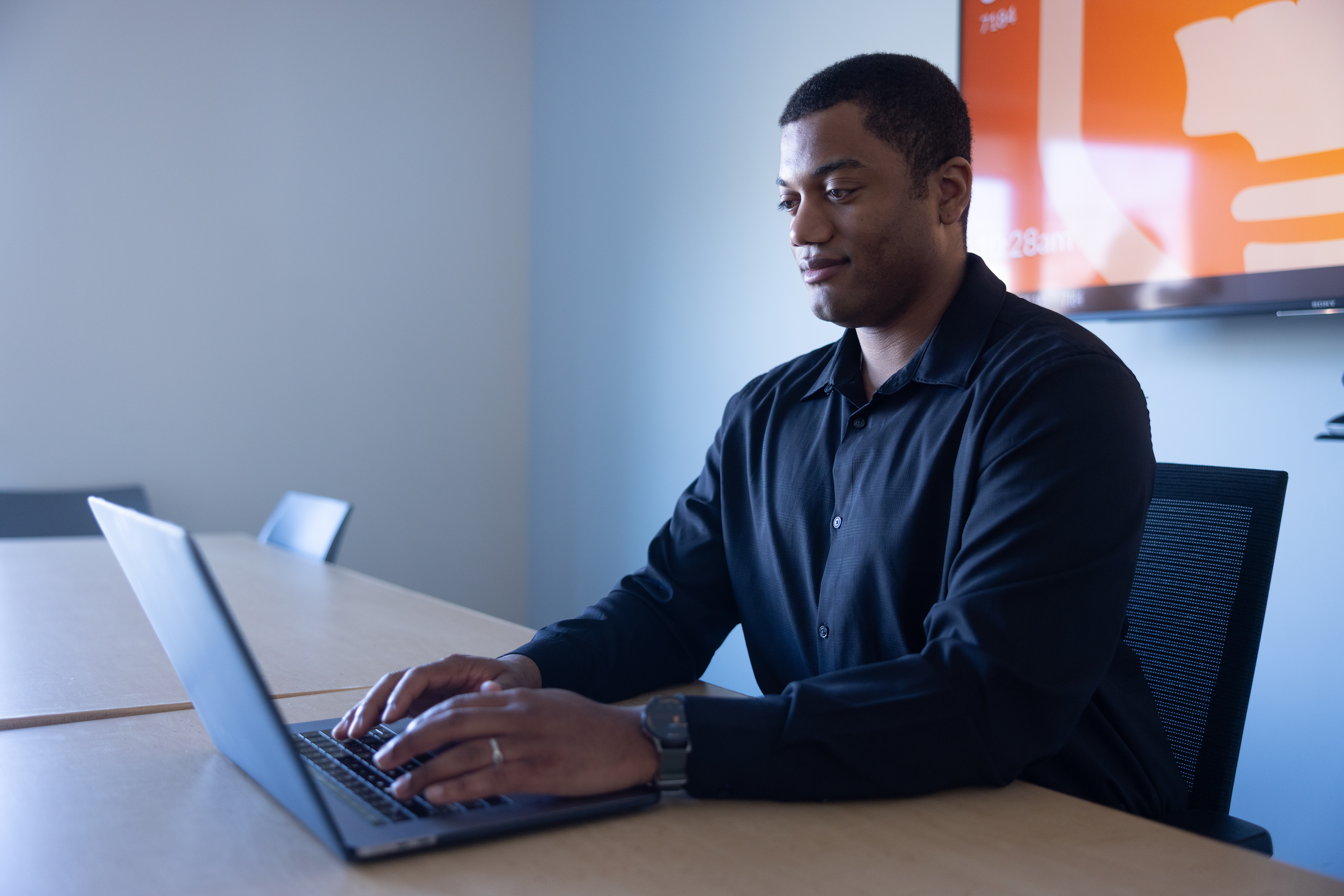man sitting at desk typing on laptop